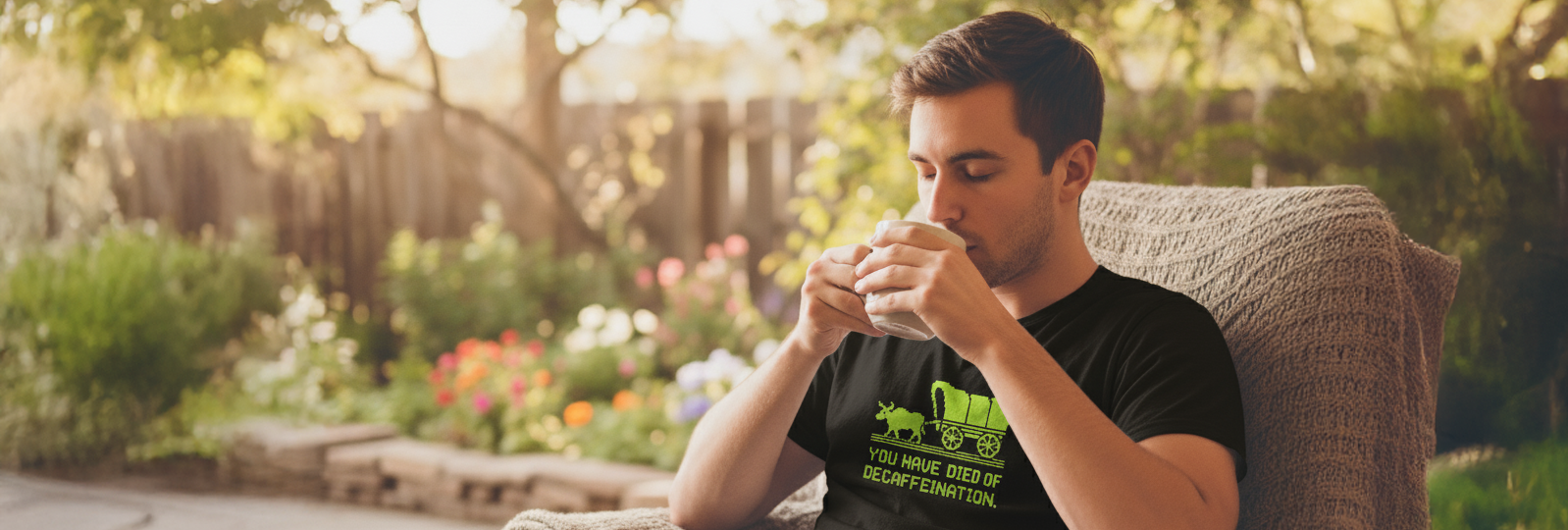 Man wearing a funny coffee t-shirt that says “You Have Died of Decaffeination,” sipping coffee outdoors — gift idea for coffee and cocktail lovers, printed in the USA by Sip & Shirt.
