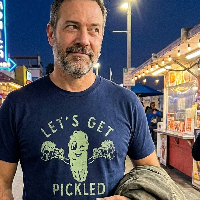 Man wearing a navy blue 'Let's Get Pickled' t-shirt at the Santa Monica Pier at night.