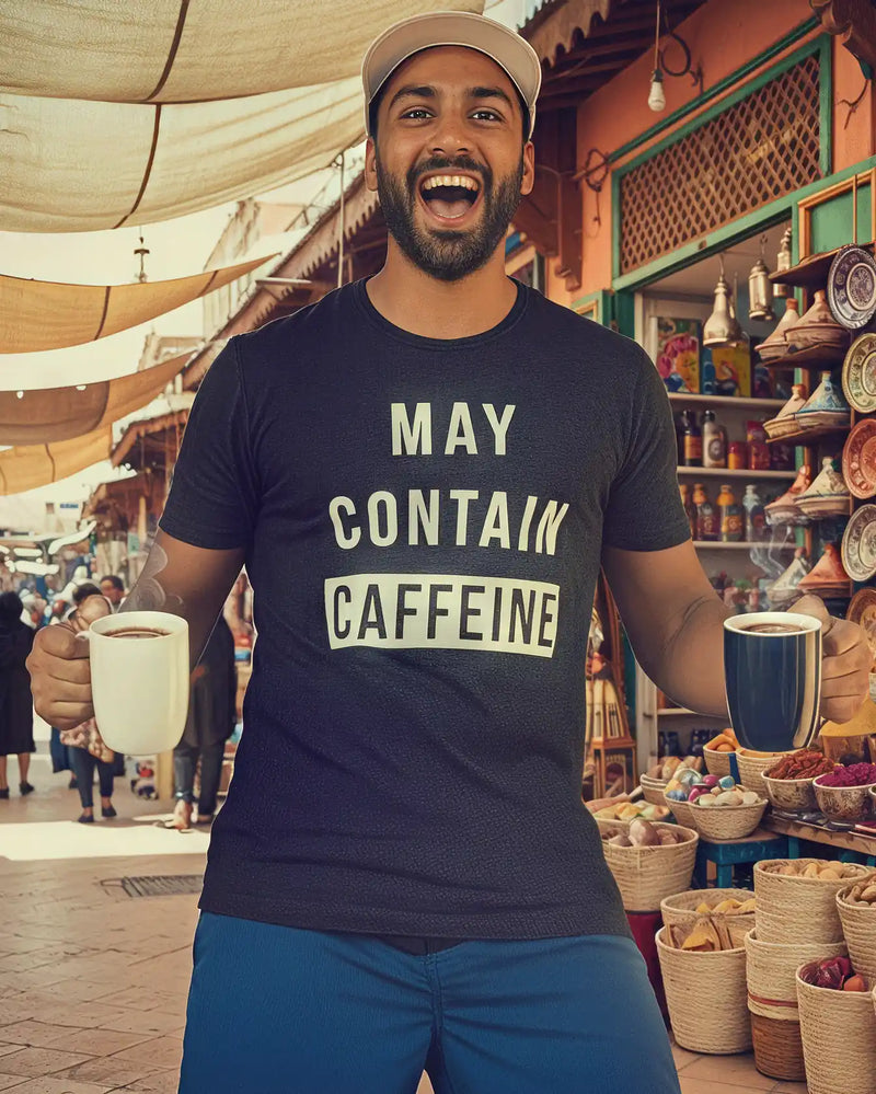 Man holding two coffee mugs and laughing in a market, wearing a funny men’s coffee shirt that says “May Contain Caffeine” by Sip & Shirt.