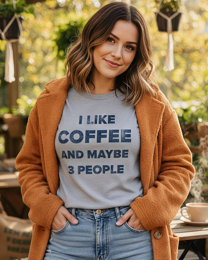 Woman smiling at café wearing a funny coffee t-shirt that says “I Like Coffee and Maybe 3 People” by Sip & Shirt.
